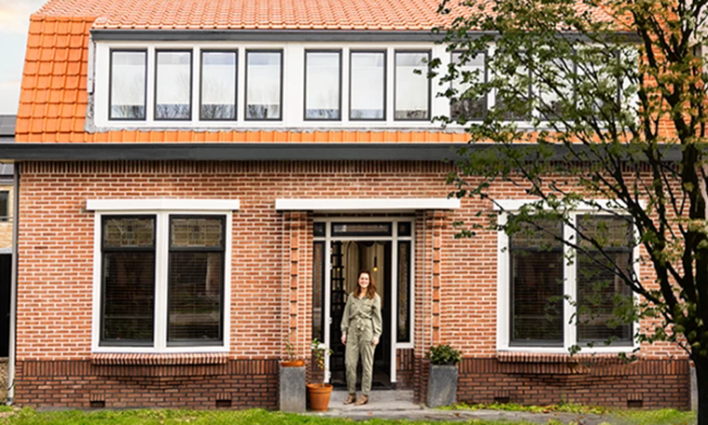 Vrouw staat in de voortuin van haar eigen woning.