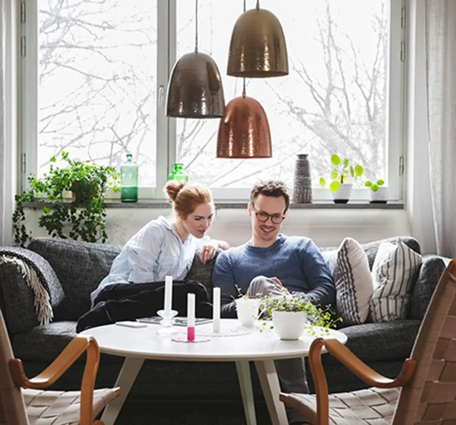 Een stel zit lachend op de bank en bekijken iets op hun mobiel.